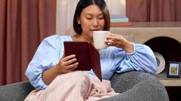donna seduta in poltrna sorseggia da tazza binca e legge da kindle con copertina rossa