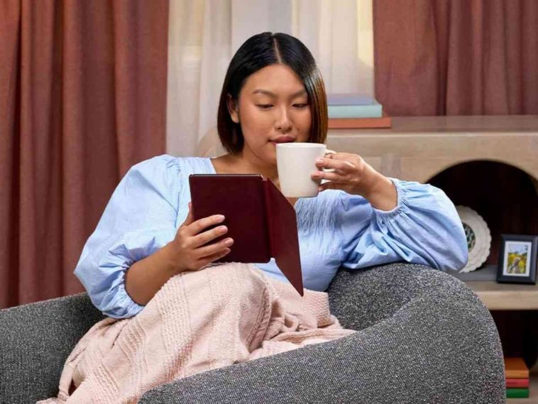 donna seduta in poltrna sorseggia da tazza binca e legge da kindle con copertina rossa