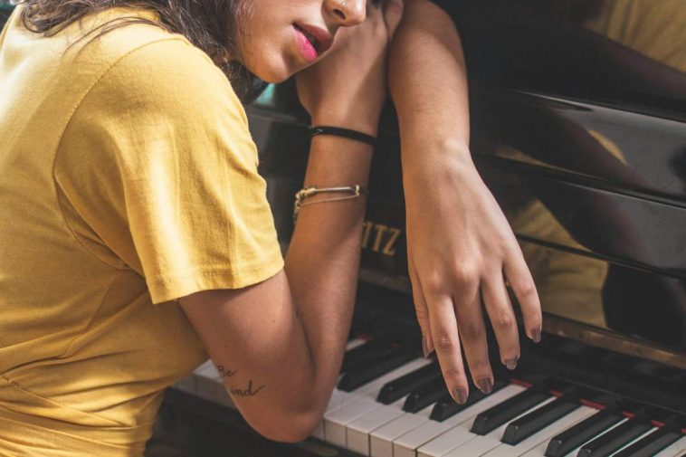 Una pianista con la maglia gialla appoggiata al pianoforte