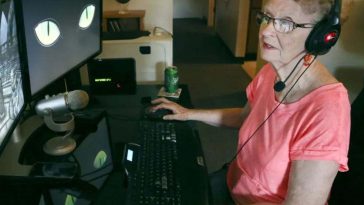 signora anziana con cuffie da gaming seduta alla scrivania con schermo computer davanti