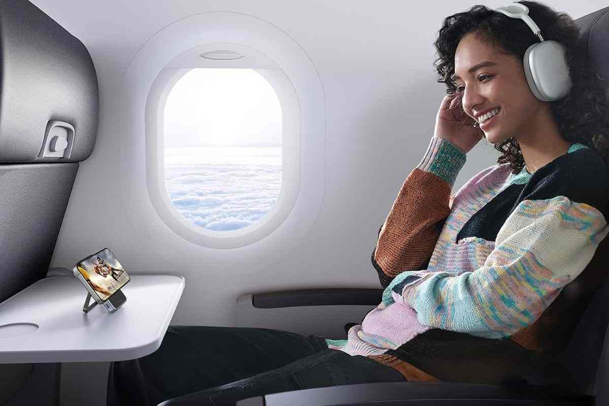 ragazza con cuffie in aereo, powerbank appoggato davanti a lei su tavolinetto