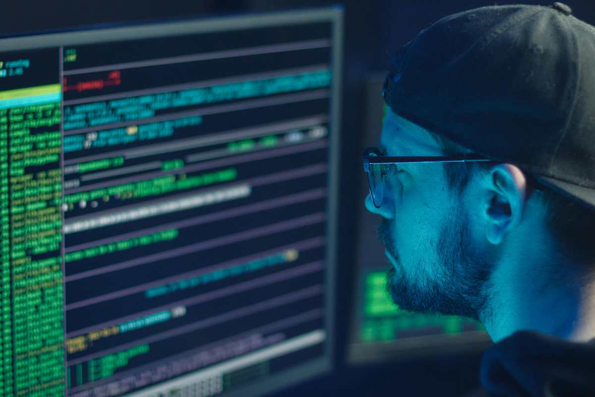 Un ragazzo con gli occhiali di fronte a uno schermo di un pc occupato da codici