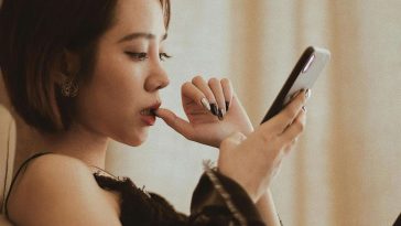 Una ragazza con un dito in bocca che guarda il telefono