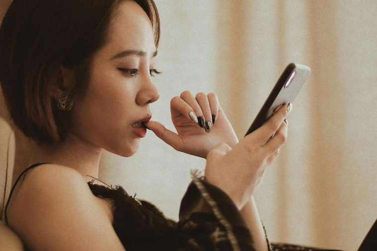 Una ragazza con un dito in bocca che guarda il telefono