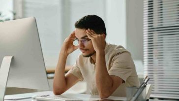 uomo che si tiene la testa davanti al pc