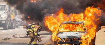 Un'auto in fiamme con un vigile del fuoco