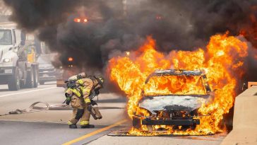 Un'auto in fiamme con un vigile del fuoco