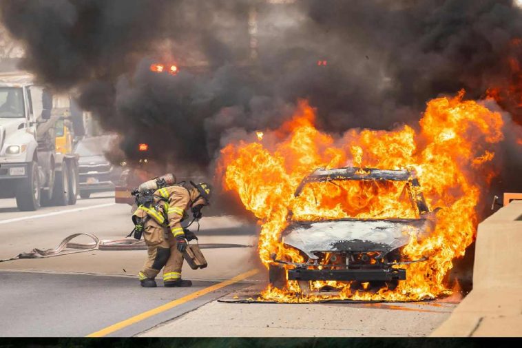 Un'auto in fiamme con un vigile del fuoco