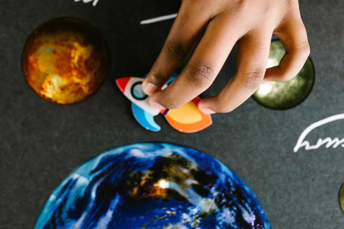 Un bambino muove un'astronave giocattolo su foglio su cui sono disegnati i pianeti