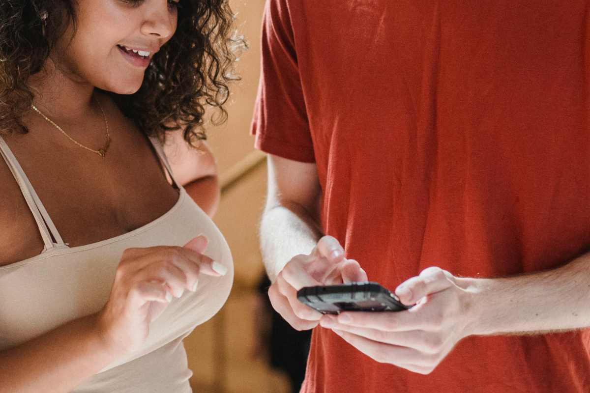 Una ragazza che assiste un giovane che scrive un messaggio sul telefono