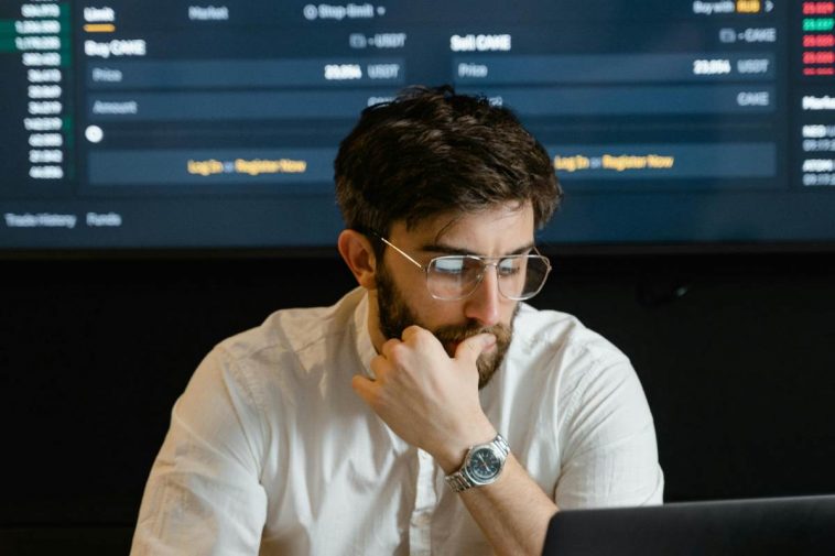 Un ragazzo con gli occhiali al computer con alle spalle delle proiezioni finanziarie