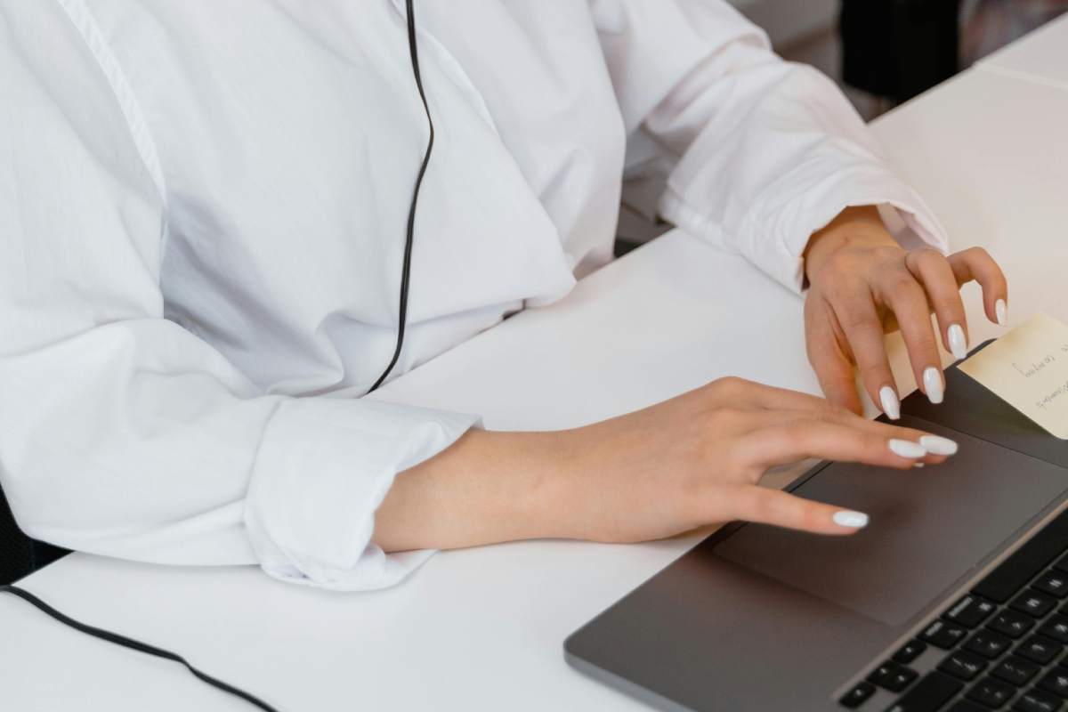 Una ragazza con una camicia bianca che batte un testo sulla tastiera di un laptop
