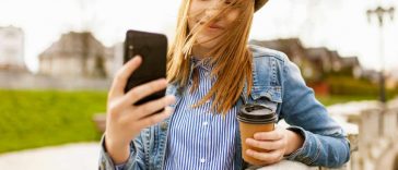 Una ragazza con un cappello e un bicchiere di caffè con un telefono fra le mani