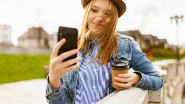 Una ragazza con un cappello e un bicchiere di caffè con un telefono fra le mani