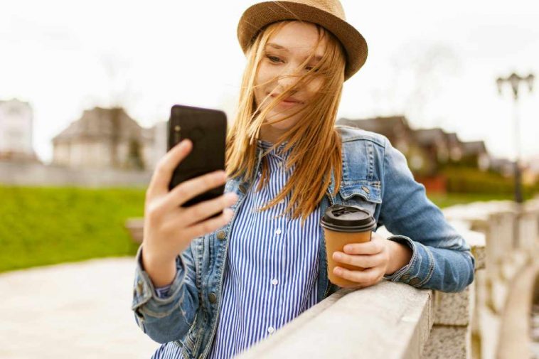 Una ragazza con un cappello e un bicchiere di caffè con un telefono fra le mani