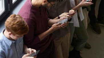 Ragazzi in fila con la testa piegata sui telefonini