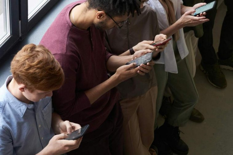 Ragazzi in fila con la testa piegata sui telefonini