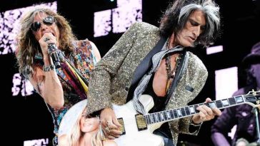 chitarrista ( joe perry) con capelli neri e bianchi, giacca maculata e chitarra bianca con immagine di ragazza, cantante (Steven Tyler) con occhiali da sole micrfono in mano