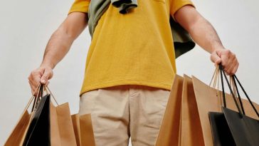 Un uomo con una polo gialla e tante buste in mano dopo lo shopping