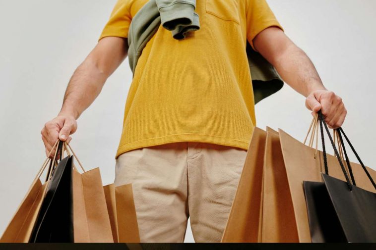 Un uomo con una polo gialla e tante buste in mano dopo lo shopping