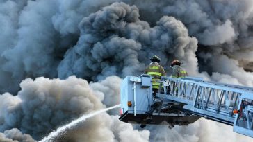 Dei vigili del fuoco su una gru circondati dal fumo