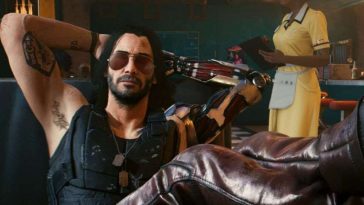 personaggio con occhiali da sole, capelli lunghi, un braccio robotico che tiene le gambe incrociate su tavolo