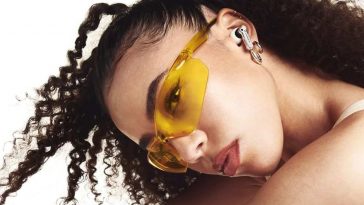 ragazza con capelli ricci, occhiali gialli, cuffie auricolari alle orecchie