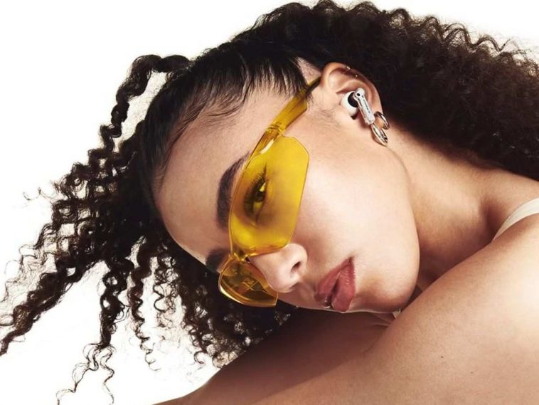 ragazza con capelli ricci, occhiali gialli, cuffie auricolari alle orecchie