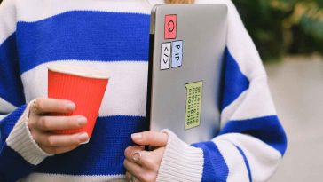 Una ragazza con un maglione a righe e un portatile sotto braccio