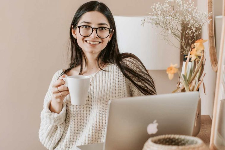 Una ragazza sorridente al computer con una tazza in mano