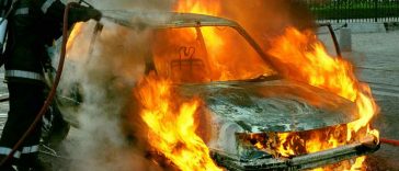 Una macchina in fiamme con un vigile del fuoco