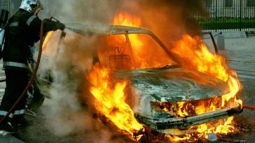 Una macchina in fiamme con un vigile del fuoco