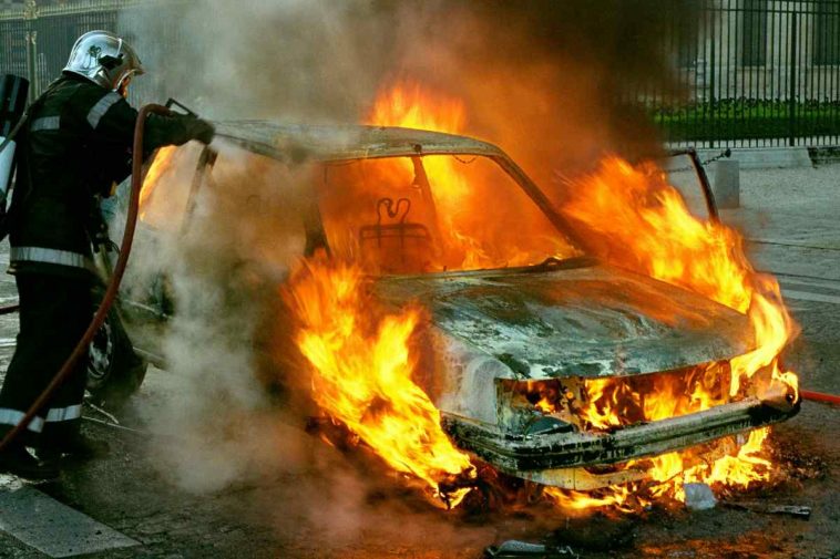 Una macchina in fiamme con un vigile del fuoco