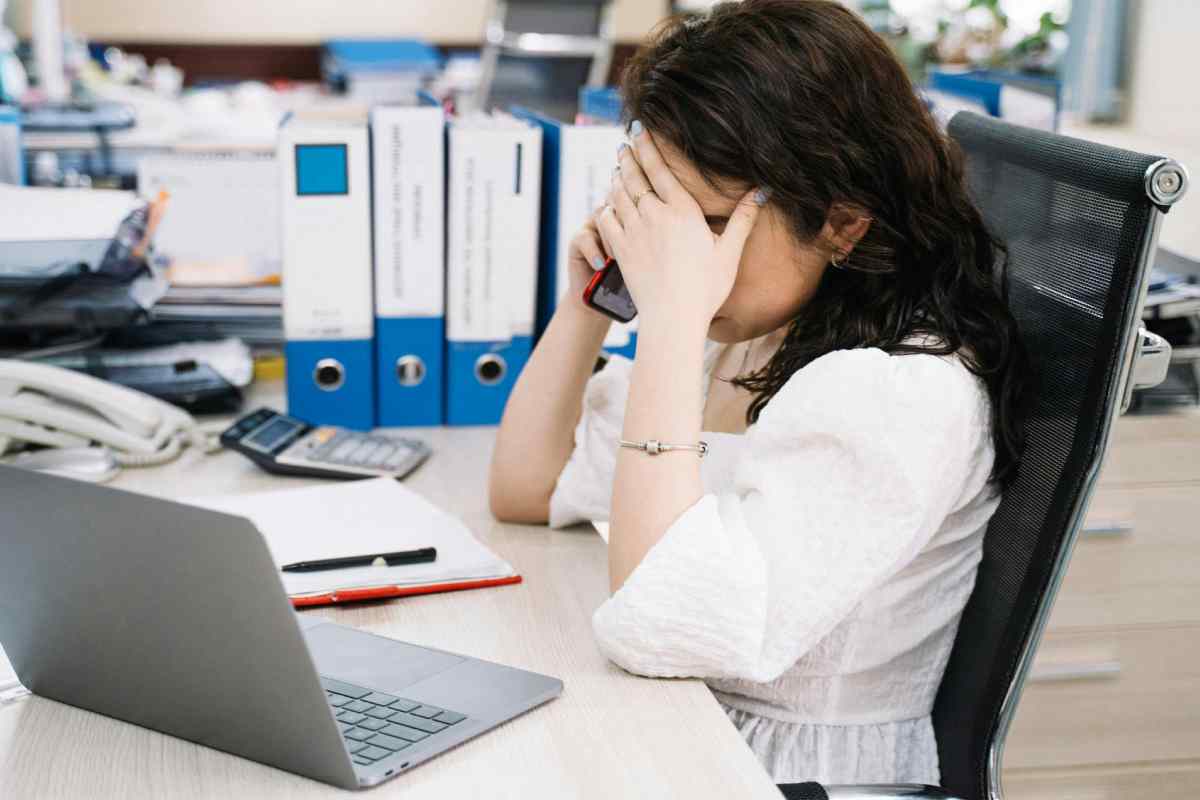 Un'impiegata che parla al telefono e si regge la fronte con una mano