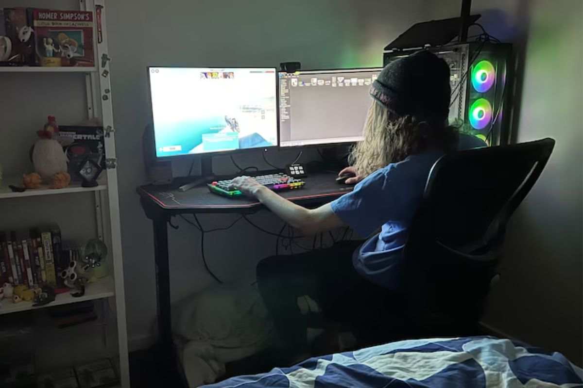 persona con capello seduto davanti due schermi PC