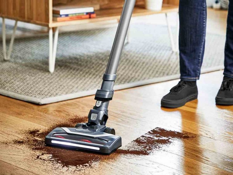 persona pulisce caffè da pavimento in legno con aspirapolvere elettrico