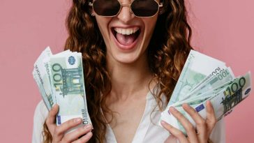 Ragazza che ride con varie banconote da 100 euro nelle mani