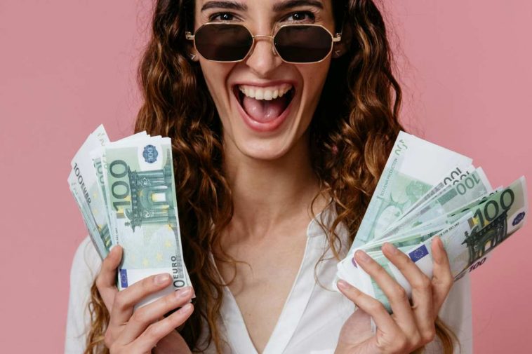 Ragazza che ride con varie banconote da 100 euro nelle mani