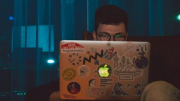 Un ragazzo con gli occhiali che lavora al portatile in una stanza buia