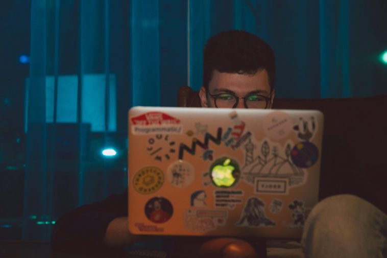 Un ragazzo con gli occhiali che lavora al portatile in una stanza buia