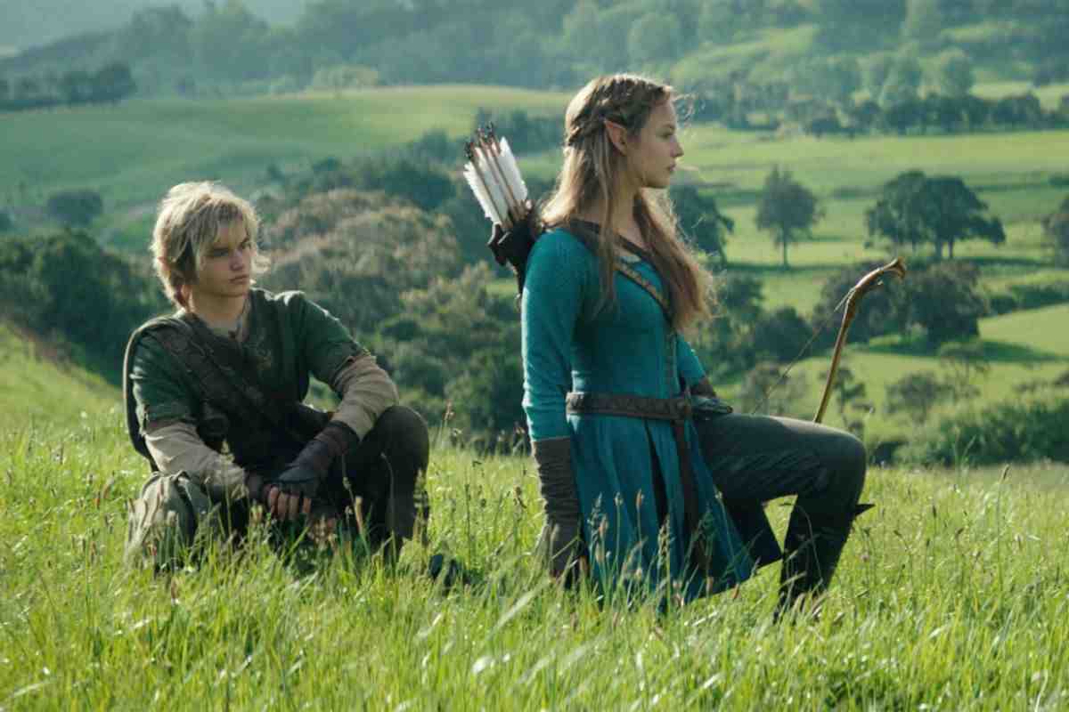 attore mascho sedto per terra con casacca verde, attrice donna n ginocchio con casacca blu arco e frecce