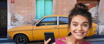 donna che indica telefonino e auto vecchia gialla sullo sfondo