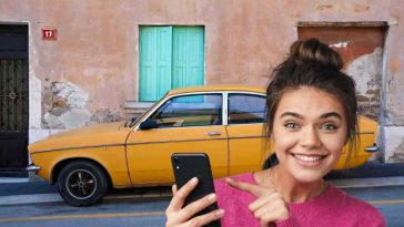 donna che indica telefonino e auto vecchia gialla sullo sfondo