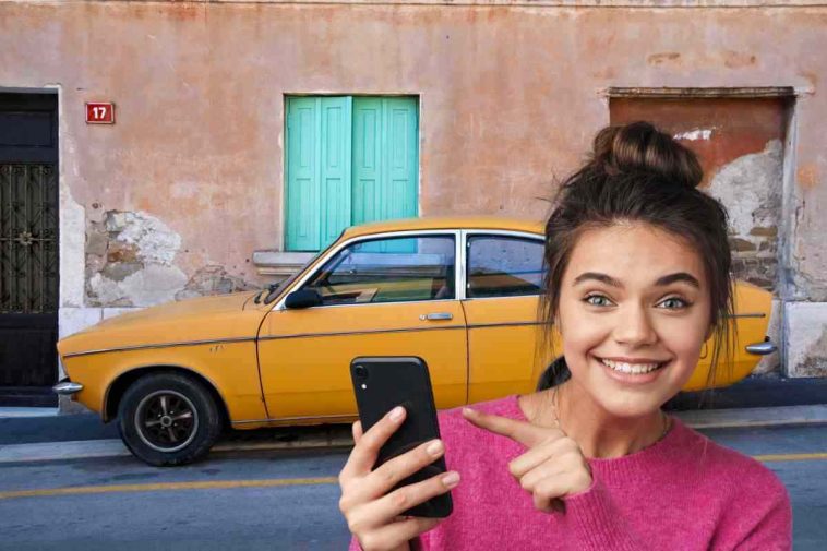 donna che indica telefonino e auto vecchia gialla sullo sfondo