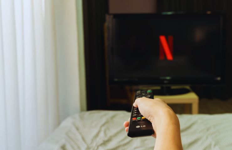 persona che indica con il telecomando una tv con logo Netflix