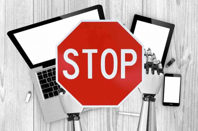 mani di robot su computer e cartello stop