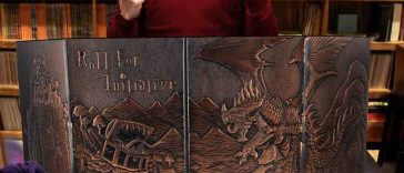 ragazzo con maglietta rossa davanti a schermo del master con ilustrazione dragon e mimic, cartelle da giocatori