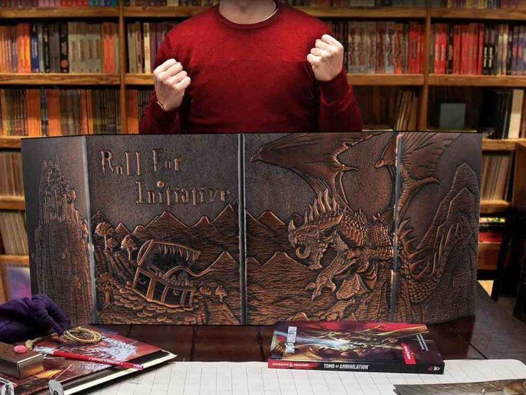 ragazzo con maglietta rossa davanti a schermo del master con ilustrazione dragon e mimic, cartelle da giocatori