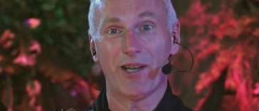 uomo con capelli bianchi e micrfono con corazza